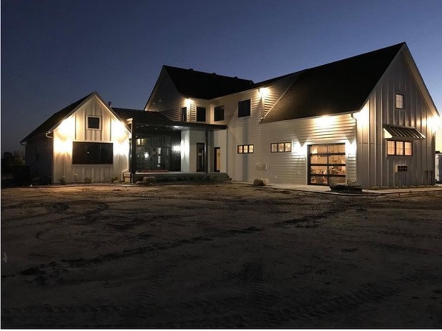 Modern farmhouse exterior with board-and-batten siding and black window frames at night
