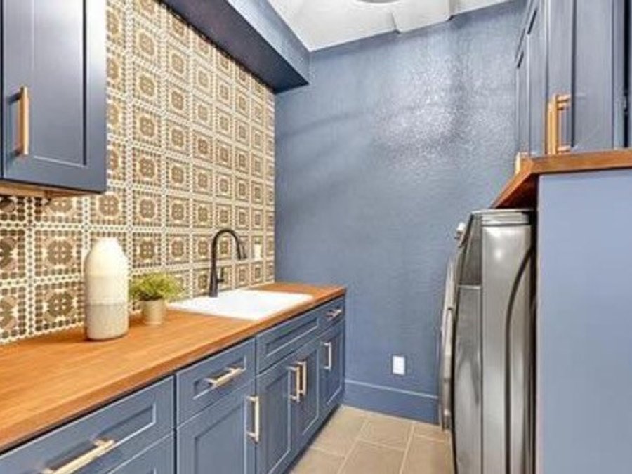 Laundry room with blue shaker cabinets, butcher-block countertop, and decorative tile backsplash