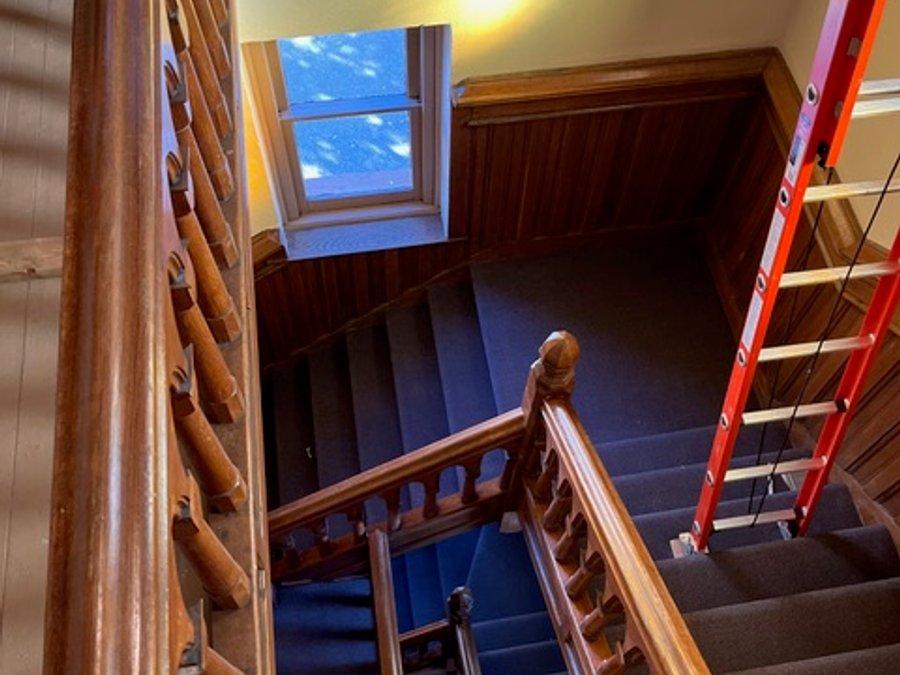 Historic cathedral staircase restoration with dark carpet runner and skylight