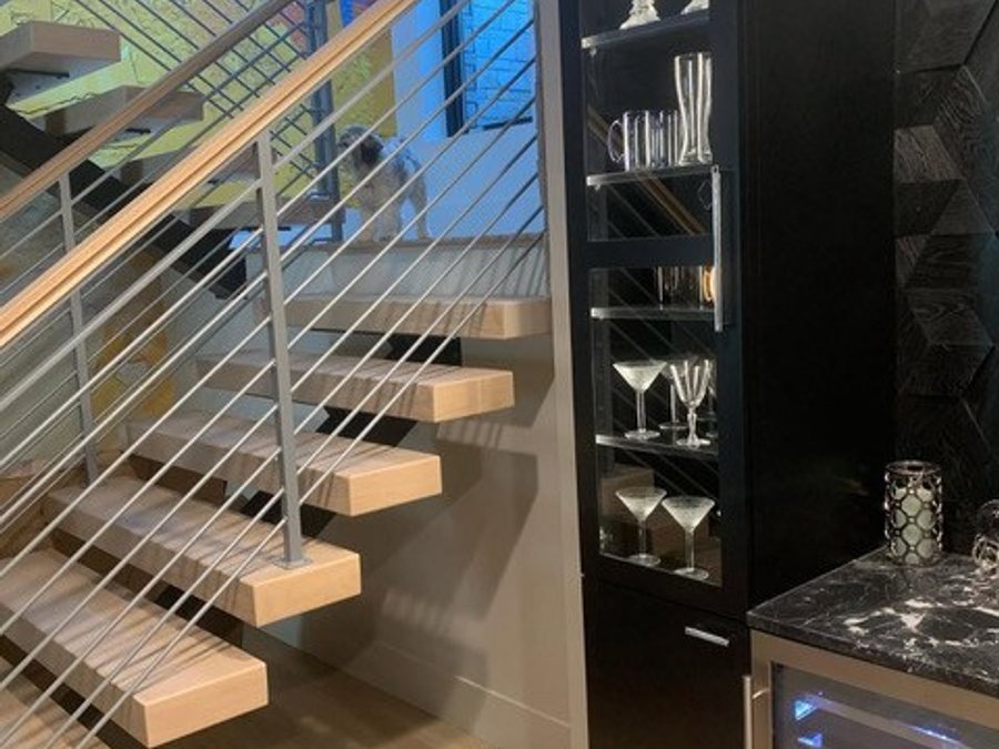 Basement bar with a floating staircase, cable railing, glass display cabinet, and wine fridge