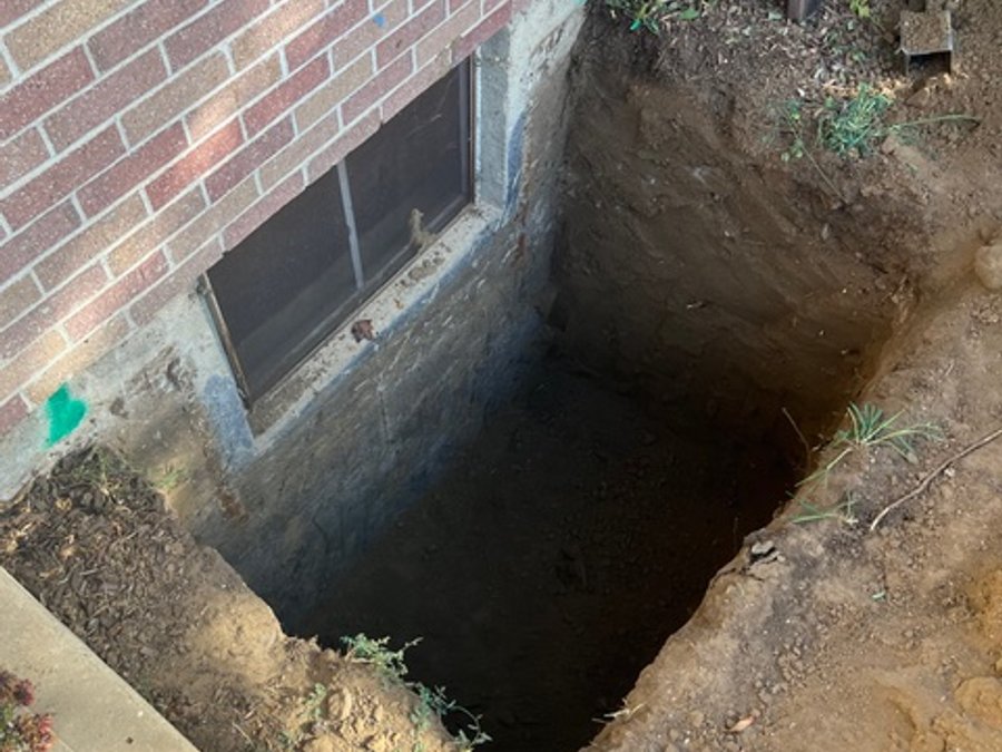 Egress window well excavation at a brick foundation exterior
