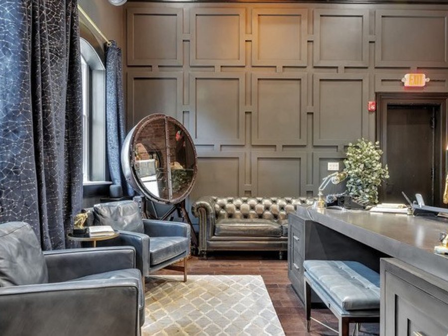 Office reception area with coffered wall paneling, a leather Chesterfield, and exposed brick