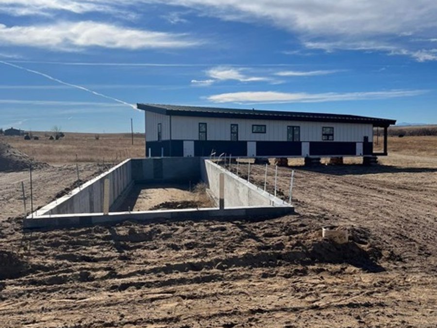 Poured concrete foundation walls with the set modular home in the background on the Colorado plains
