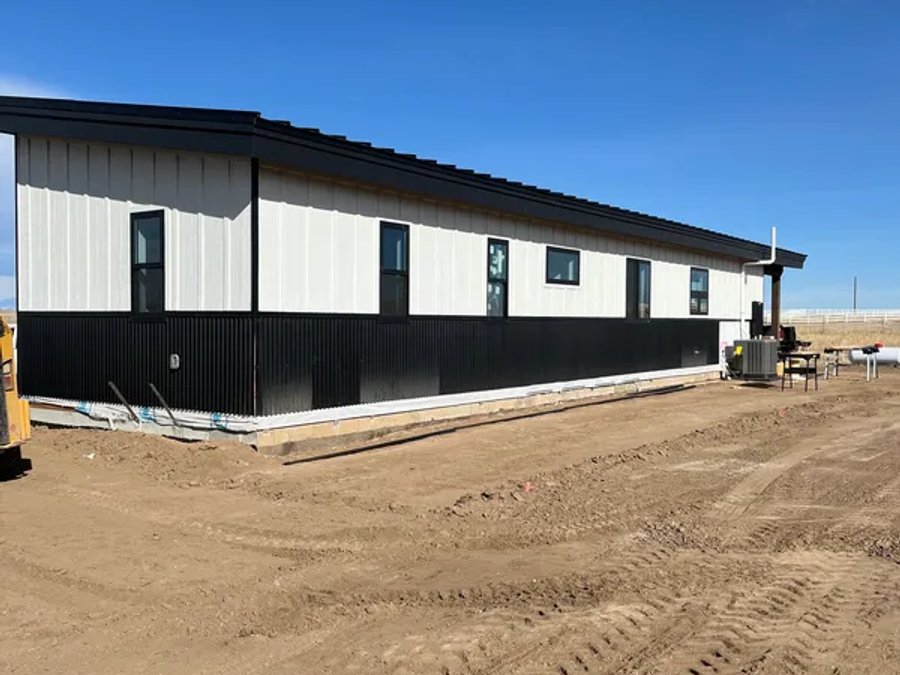Finished modular home with board-and-batten siding, metal roof, and dark skirting on a Colorado site